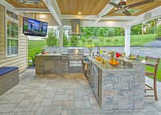 an outdoor kitchen with grill and television on the wall