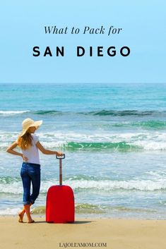 a woman standing on the beach with her suitcase and hat over her head, looking out at the ocean