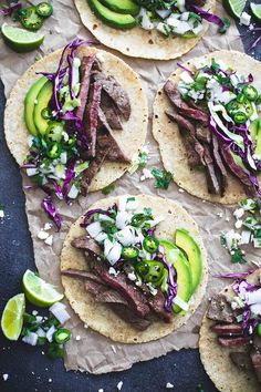 four steak tacos with shredded cabbage, avocado and cilantro on parchment paper