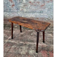 an old wooden table sitting in front of a brick wall with no one around it