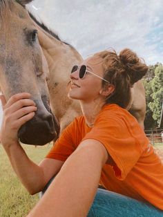 a woman in an orange shirt petting a horse