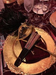 a fancy table setting with red and gold plates, silverware, and black feathers