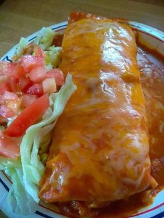 a burrito and salad on a plate with sauce, lettuce and tomato