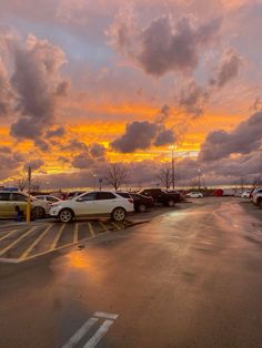 a parking lot filled with lots of parked cars under a cloudy blue and orange sky