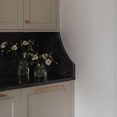 some white flowers are in vases on a black counter top with gold trim around the edges