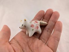 a small white cat figurine sitting on someone's hand