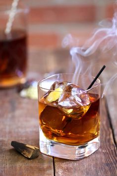 two glasses filled with liquid and ice sitting on top of a wooden table