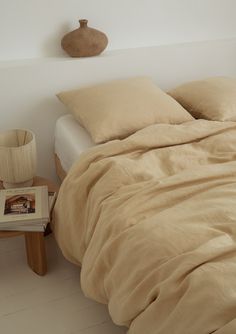 an unmade bed with two pillows and a vase on the side table next to it