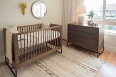 a baby crib in the corner of a room next to a dresser and window