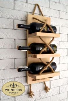 a wooden wine rack with six bottles on it and rope wrapped around the top, hanging from a brick wall