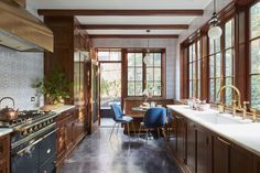 a kitchen with wooden cabinets and blue chairs next to a stove top oven in front of two windows