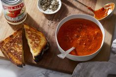 a wooden cutting board topped with a bowl of soup and two grilled cheese sandwiches