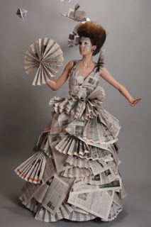 a woman in a dress made out of newspapers and holding a fan with her right hand