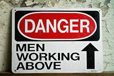 a red and black sign that says danger men working above the right hand arrow on a white wall