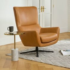 a brown leather chair sitting on top of a wooden floor next to a table with a cup