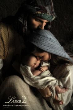 a man holding a baby wrapped in a blanket while wearing a blue hat and scarf