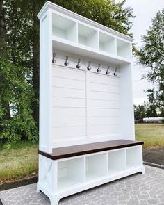 a white wooden bench with hooks on the back and two benches below it in front of some trees