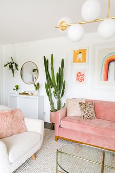 a living room with pink couches and pictures on the wall above them, along with potted cacti