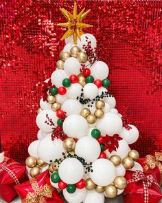 a christmas tree made out of balloons and other holiday decorations on a red sequin background