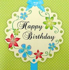 a happy birthday card with blue ribbon and flowers on it's corner, in front of a green polka dot background