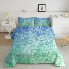 a bed with blue and green comforters in a room next to a white chair