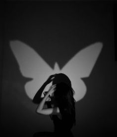 a woman standing in front of a wall with a butterfly shadow on it's back