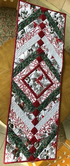 a quilted christmas table runner on top of a wooden chair next to a potted plant