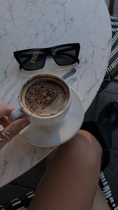 a cup of coffee sitting on top of a white saucer next to a pair of black sunglasses