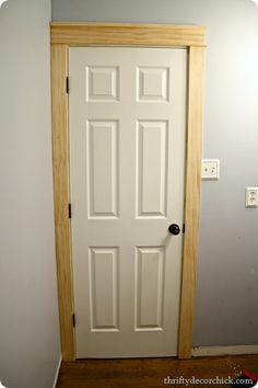 an empty room with a white door and wood frame around the bottom part of the door