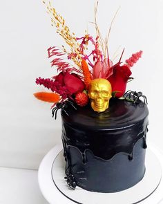 a black cake with a gold skull on top and red flowers in the middle is sitting on a white plate