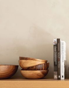 three wooden bowls sitting on top of a shelf next to a book and two books