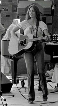 a woman holding a guitar while standing in front of other people and playing music instruments