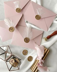 pink envelopes with gold and white feathers on them, next to some other items