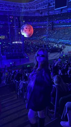 a woman standing in front of an audience at a concert with the moon behind her