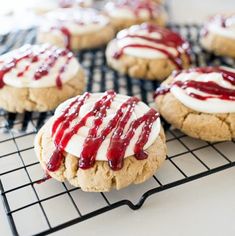 cookies with white frosting and red sauce on top are cooling on a wire rack