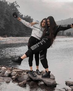 two young women standing on rocks by the water with their arms around each other and pointing at something