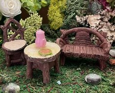 two miniature chairs and a table made out of tree stumps with flowers in the background