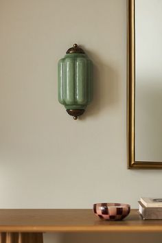 a green vase sitting on top of a wooden table next to a mirror and book