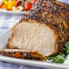 a piece of meat sitting on top of a white plate next to a bowl of salad