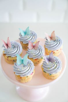 cupcakes with frosting and butterflies on a pink cake platter, ready to be eaten