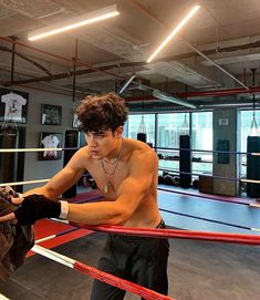 a shirtless young man standing next to a boxing ring holding a glove in his hand