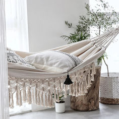 a white hammock with tassels hanging from it's sides in front of a window