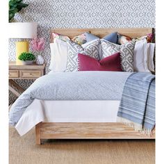 a bed with pillows and blankets on top of it next to a nightstand in front of a wallpapered wall