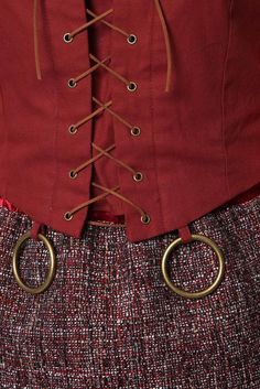 a woman wearing a red jacket and skirt with gold rings on the waist, in front of