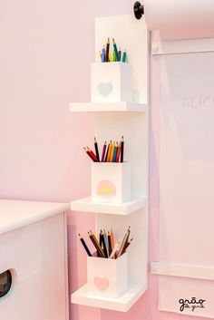 a white shelf filled with lots of pencils and markers next to a pink wall