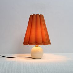 an orange lamp sitting on top of a table next to a white wall and floor