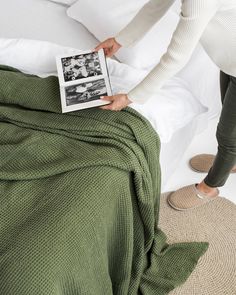 two people standing over a bed with a green blanket on top of it and an open magazine in front of them