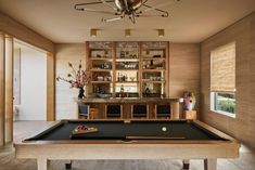 a pool table in the middle of a room with an entertainment center and bar behind it