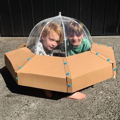 two young boys sitting in a cardboard box shaped like a spaceship with blue dots on it