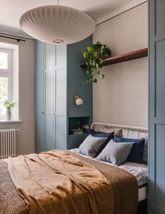 a bed sitting under a window next to a wooden shelf filled with pillows and blankets